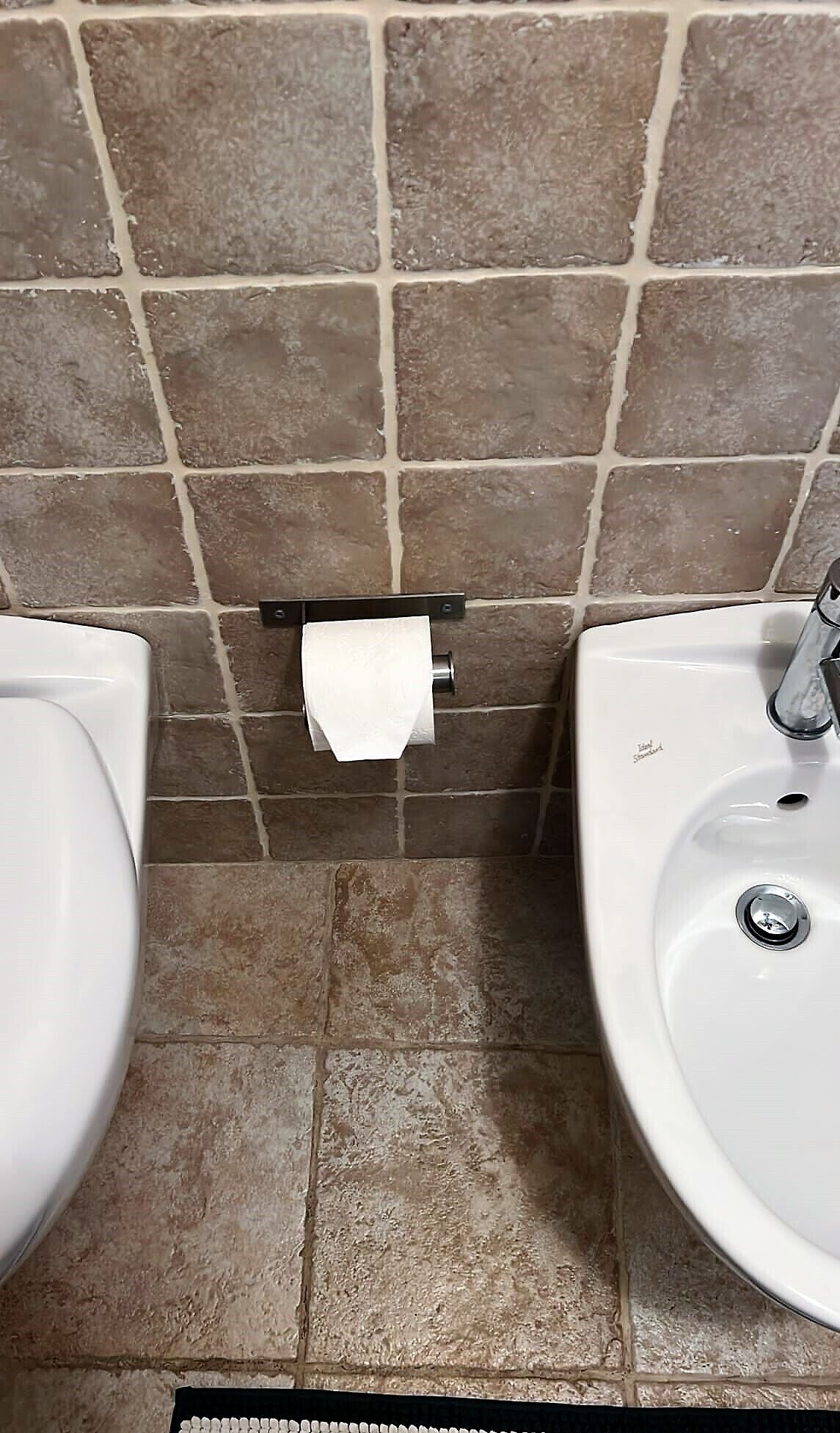 Une salle de bain avec deux lavabos, un porte-rouleau de papier toilette et des murs recouverts de carreaux bruns.