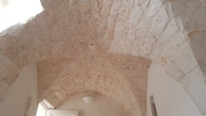 Eine gewölbte Decke mit rauen Steinwänden, einer weißen Tür und einem kleinen Fenster.