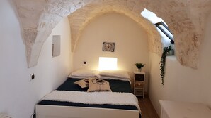 Ein schmales Zimmer mit einem Bett, einem kleinen Nachttisch, einer Wandablage und einem Fenster mit Blick.