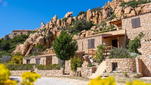 A stone building with a balcony, surrounded by rocky terrain and greenery. - Residence La Falata (Trinità d'Agultu e Vignola)
