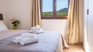 A hotel room with a bed, a window with curtains, a plant, and towels on the bed. - Residence La Falata (Trinità d'Agultu e Vignola)