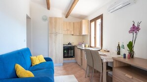 A modern kitchen with wooden cabinets, a dining area with a table and chairs, and a blue sofa with yellow cushions. - Residence La Falata (Trinità d'Agultu e Vignola)