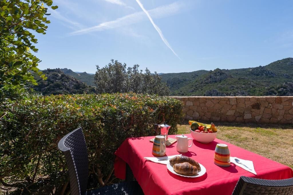 Disposição para refeições ao ar livre com uma mesa posta para dois, uma cesta de frutas e uma vista panorâmica das colinas ao fundo.