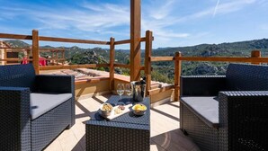 An outdoor seating area with wicker furniture and a table set with food and drinks, overlooking a mountainous landscape. - Residence La Falata (Trinità d'Agultu e Vignola)
