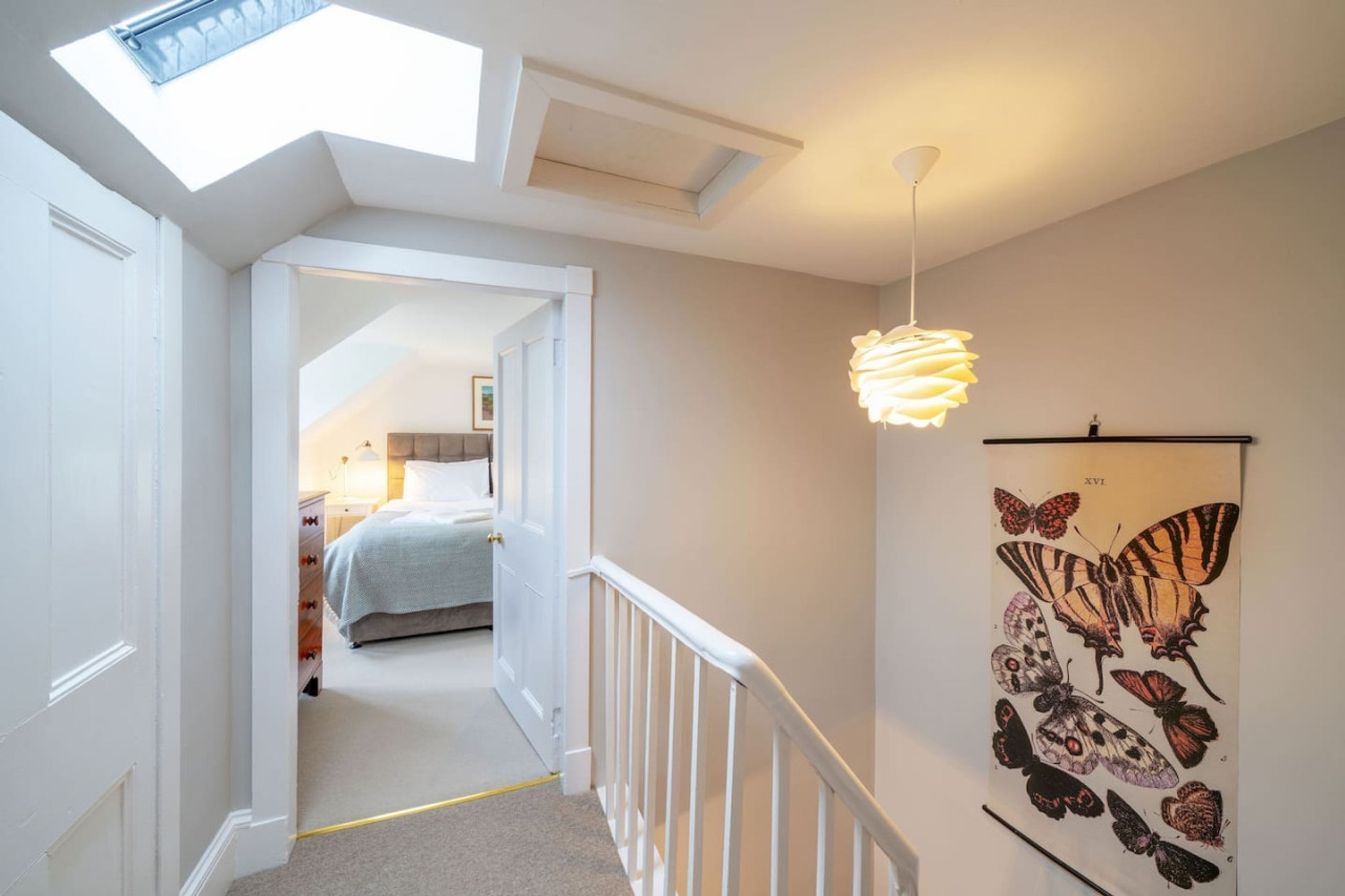 A narrow hallway with a skylight, a bed in the background, and a butterfly wall art.