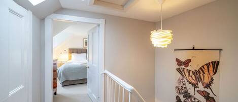 A narrow hallway with a skylight, a bed in the background, and a butterfly wall art.