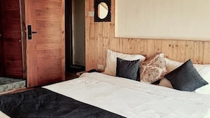 Une chambre avec un plafond en bois, un lit avec une literie blanche et foncée, et une porte en bois.