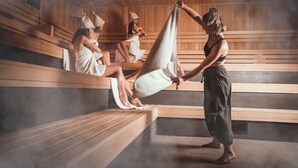 A sauna with wooden benches and a person adjusting a towel. - Ferienwohnung Kellermeister für 4 Personen in den Ferienwohnungen Bullay, Mosel (Bullay)