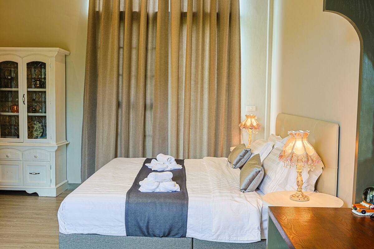 A neatly made bed with towels, a wooden nightstand with a lamp, and a white cabinet with glass doors.
