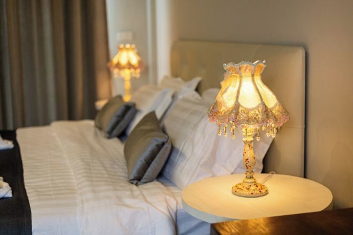 Habitación de hotel con cama, almohadas y mesita de noche con lámpara.