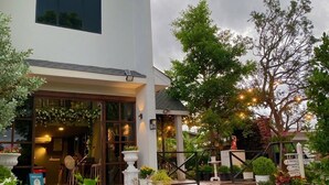A modern building with a large window, a staircase leading to the entrance, and a garden area with various plants and flowers. - Phuping Valley Resort  (Tak)