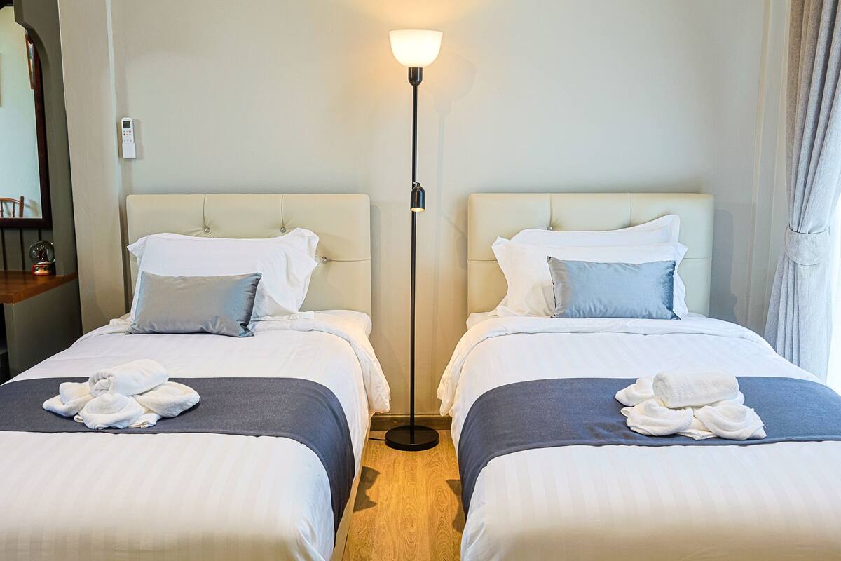 A hotel room with two beds, a standing floor lamp, and a nightstand with a lamp.