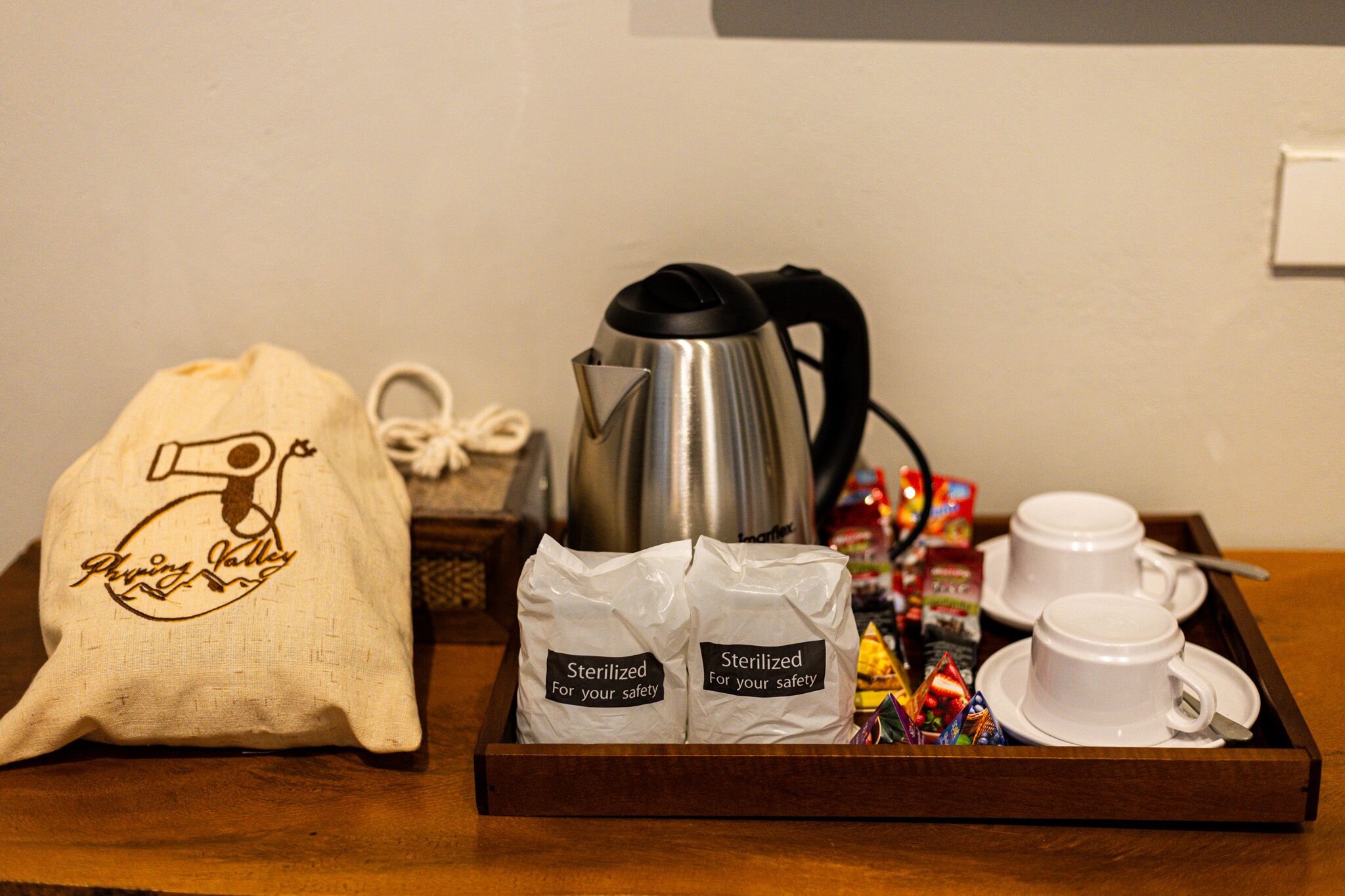 Un plateau contenant une cafetière en acier inoxydable, deux tasses blanches, un sac blanc orné d’un logo et deux sacs étiquetés « Stérilisé pour votre sécurité ».