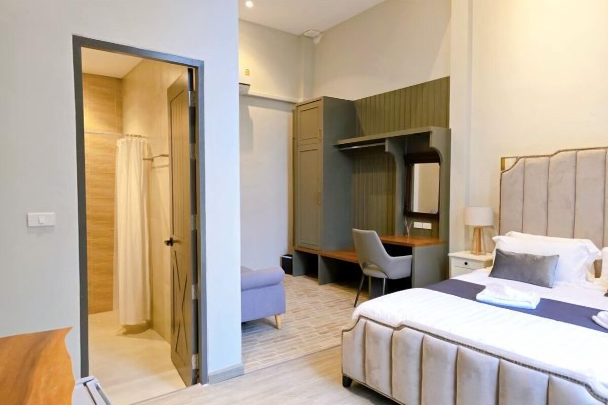 A hotel room with a bed, a desk, a chair, a wardrobe, and a shower area.