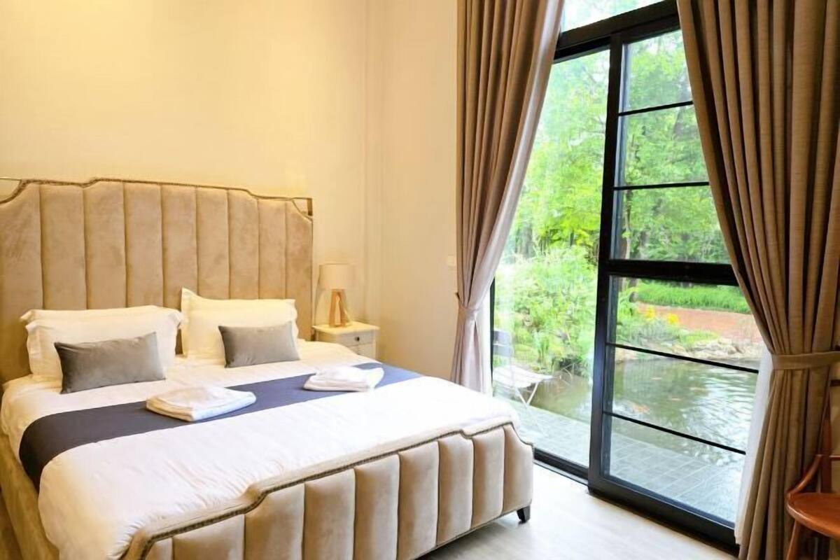 A bedroom with a large bed, a nightstand, and a window with curtains.