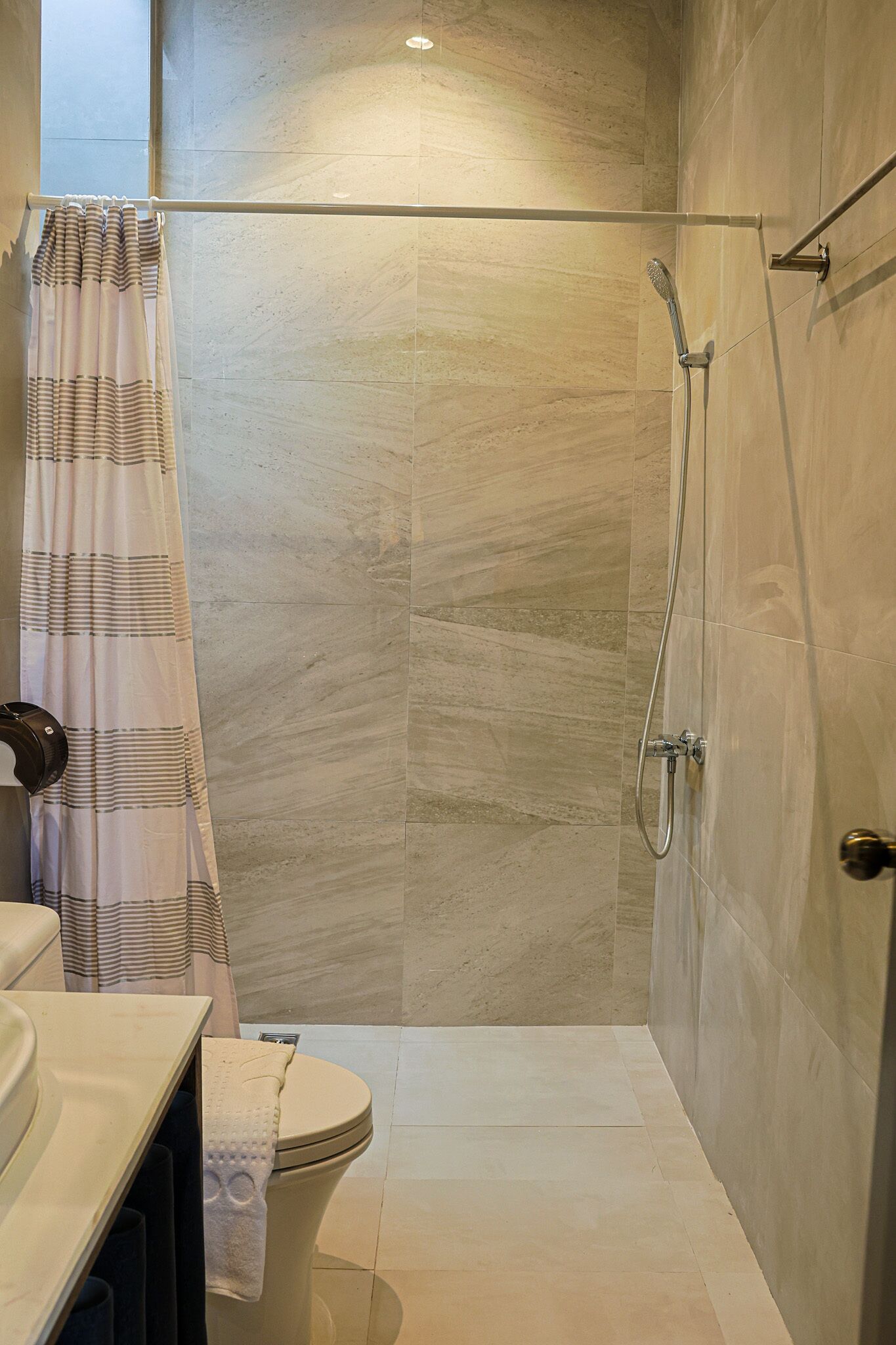 Une salle de bain avec une douche, des toilettes et une serviette accrochée au mur.