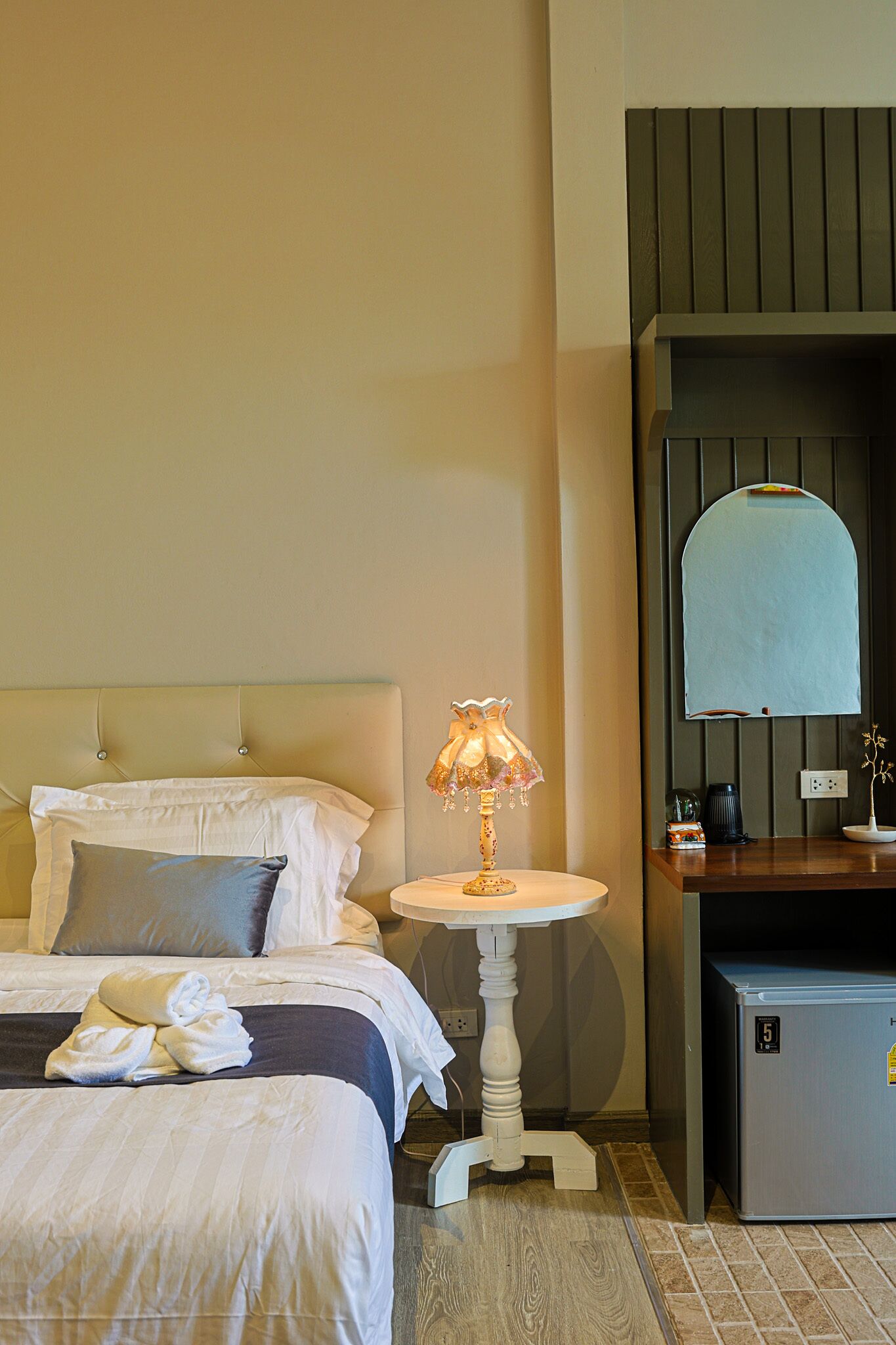 A hotel room with a bed, a bedside table with a lamp, a small desk, and a mirror.