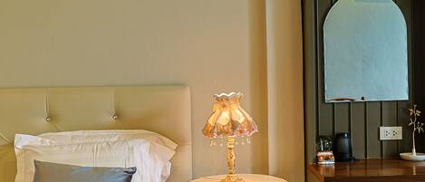 A hotel room with a bed, a bedside table with a lamp, a small desk, and a mirror.