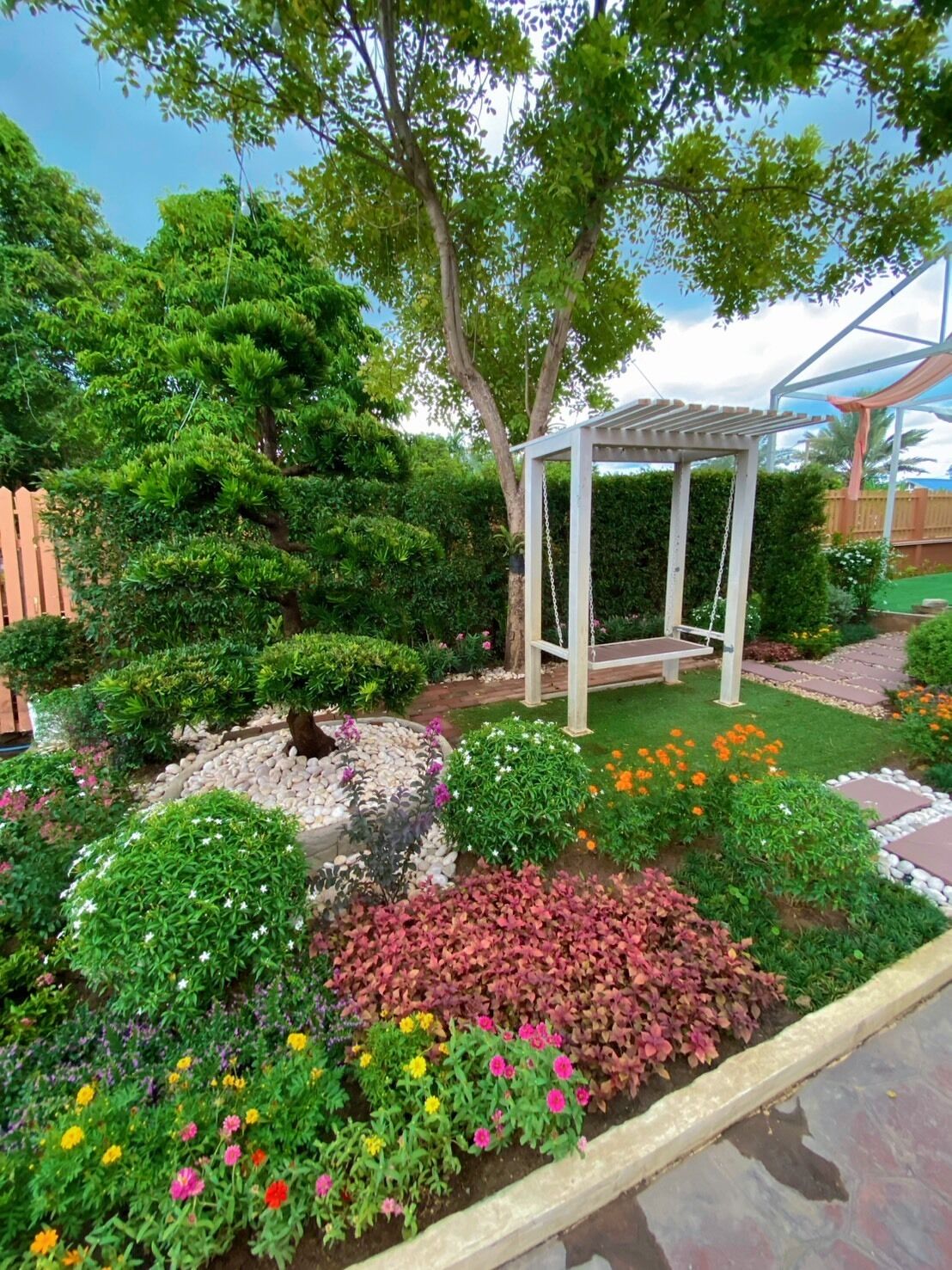 Un giardino con un gazebo, diverse piante e una recinzione in legno.