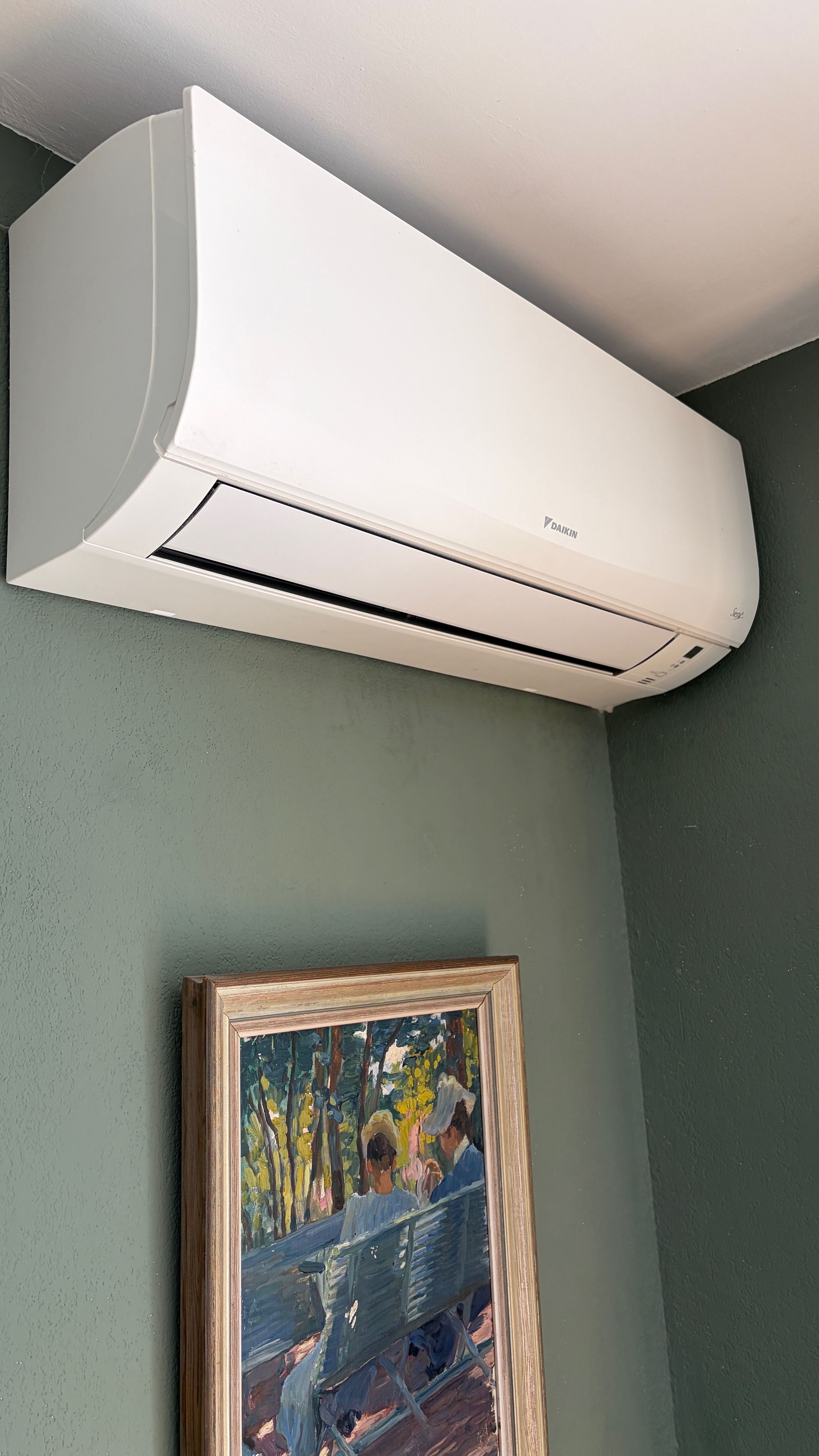 A white air conditioning unit mounted on a wall with a framed painting below it.