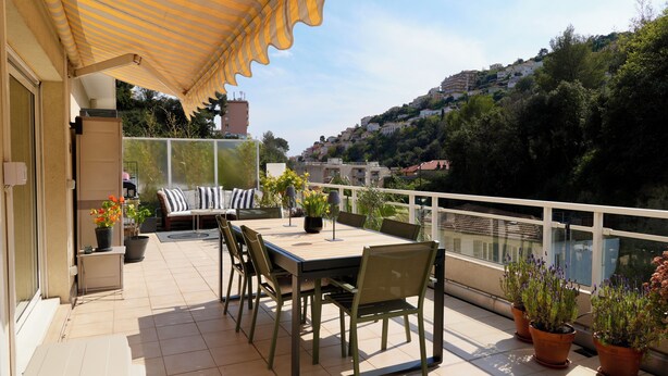 A terrace with a table and chairs, a sofa, potted plants, and a view of a hillside town. - Lovely apartment with AC and a large terrace - pool in the residence. (Nice)