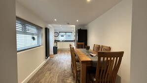 Ein enger Flur führt zu einem Essbereich mit Holztisch und Stühlen, einer Uhr an der Wand und einer Küche im Hintergrund.