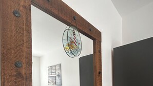 Ein Spiegel mit Holzrahmen und Buntglasdekor, der ein Schlafzimmer mit Bett, Kissen und Nachttisch reflektiert.