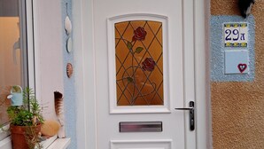 Eine weiße Tür mit Glasfenster, das ein Rosenmuster zeigt, einem Briefkasten und einem an der Wand befestigten Schild mit der Nummer 29.
