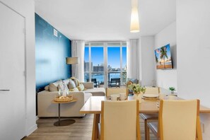A modern living room with a sofa, dining table, chairs, and a city view through large windows.
