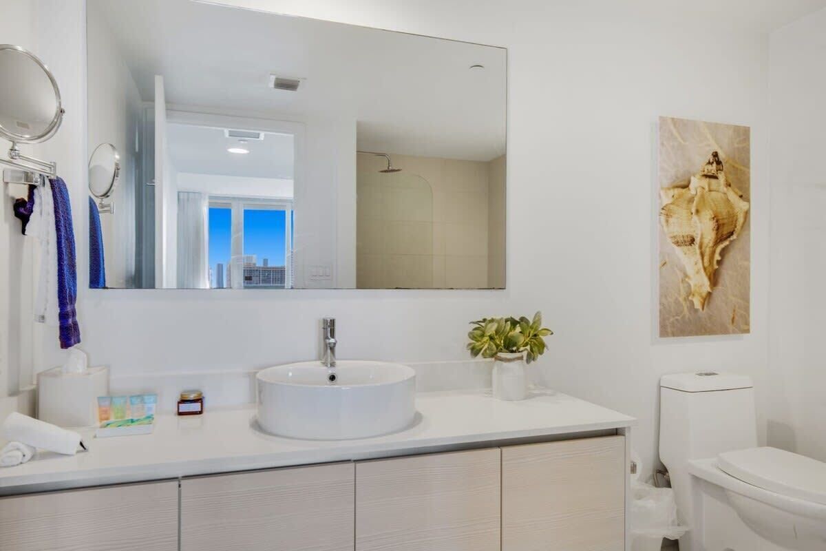 Un bany modern amb un lavabo rodó, un mirall gran, un vàter i una dutxera.