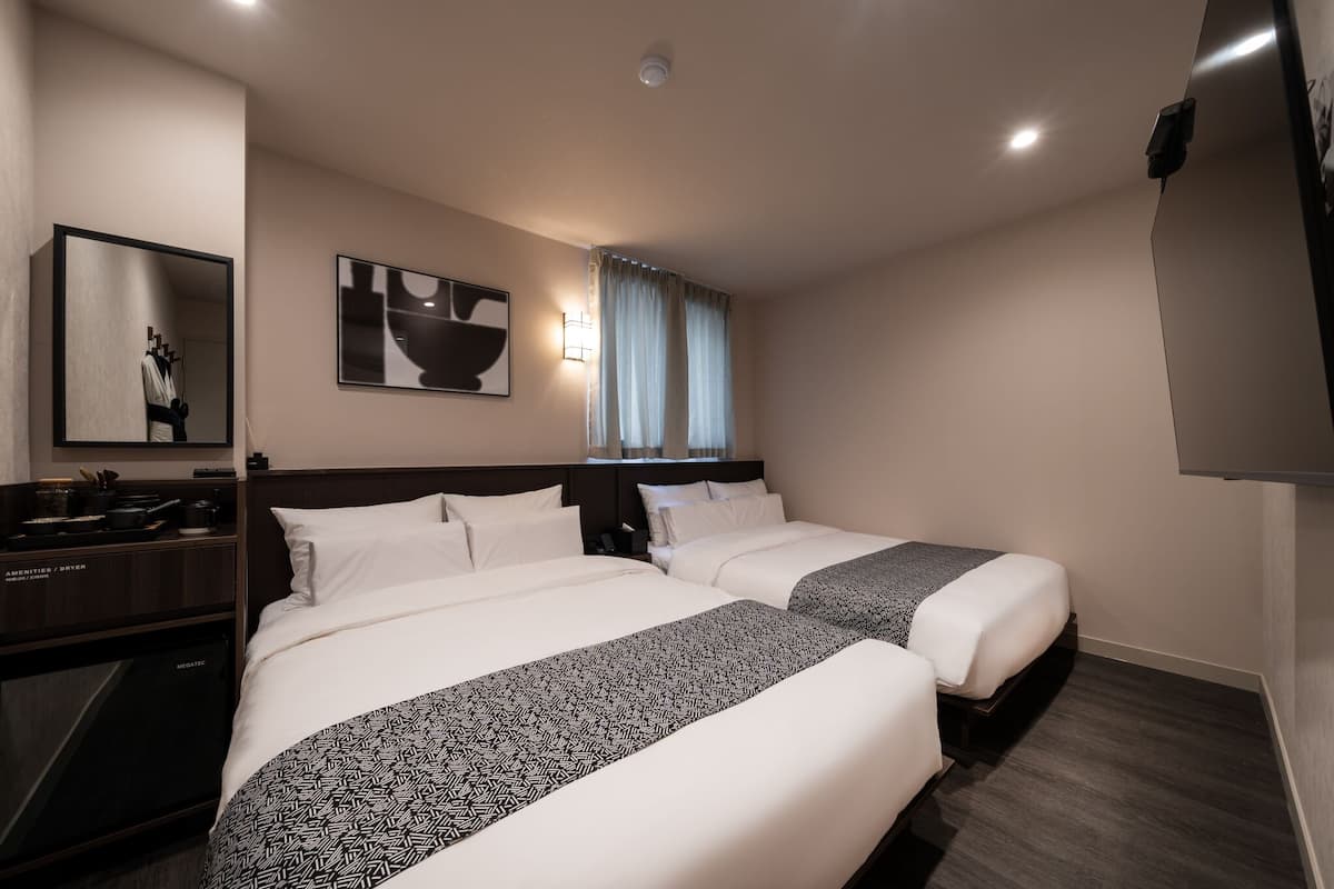 A hotel room with two beds, a desk, a mirror, and a flat-screen TV.