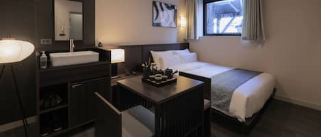 Una habitación de hotel con cama, mesita de noche, lámpara y ventana con cortinas.