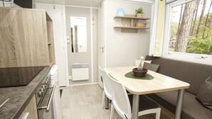 A compact kitchen with a dining area, a window with a view of trees, and built-in shelves with baskets.