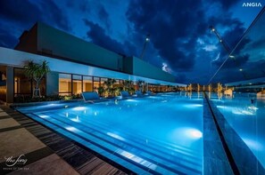 Um hotel moderno com uma grande piscina ao ar livre, área coberta com assentos e vista para o mar.