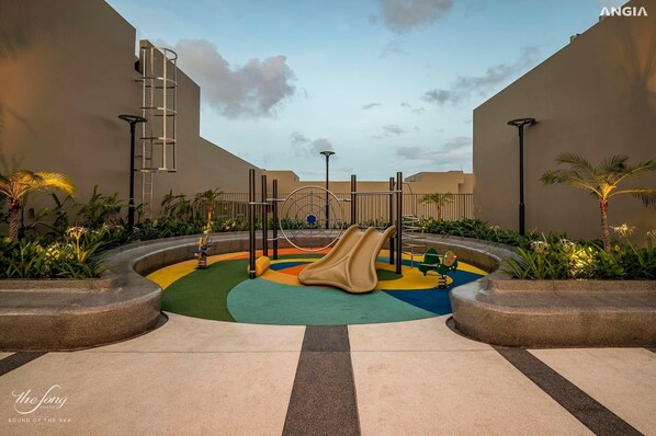 Kids can play and climb in a safe, well-equipped area surrounded by lush greenery.