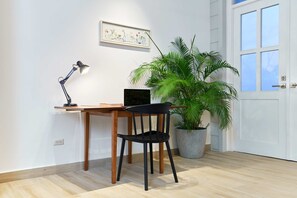Un espacio de trabajo con escritorio, silla, ordenador portátil, lámpara de escritorio y planta en maceta.