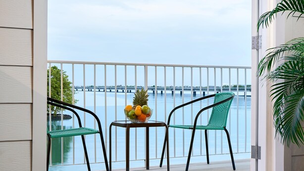 A balcony with a view of a bridge over water, two chairs, a small table with a fruit bowl, and a potted plant. - w* | Amazing 1BR w/ Balcony  & AC in San Felipe (Panamá)