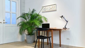 A room with a wooden desk, a black chair, a potted plant, a framed picture on the wall, and a desk lamp. - w* | Amazing 1BR w/ Balcony  & AC in San Felipe (Panamá)