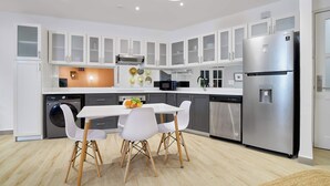 A modern kitchen with white cabinets, stainless steel appliances, and a dining area with white chairs. - w* | Amazing 1BR w/ Balcony  & AC in San Felipe (Panamá)