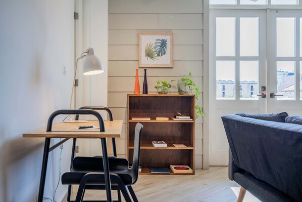 A modern living space with a desk, chairs, a bookshelf, a sofa, and a window with a city view.
