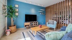 Ein Wohnzimmer mit Fernseher, einer Pflanze, einem Couchtisch und einem blauen Sofa.