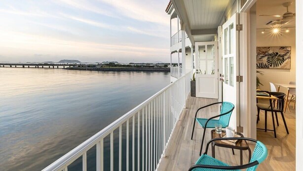 Un balcon avec vue sur l’eau, un coin repas avec des chaises et une table, et une porte donnant sur un espace intérieur.