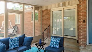 Ein überdachter Patio-Bereich mit einer Ziegelwand, einer blauen Tür und einem blauen Sofa mit gemusterten Kissen.