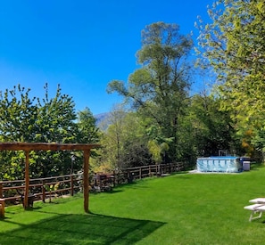 Um gramado bem cuidado com uma pérgola de madeira, área cercada e compartimento para piscina.