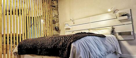 A modern bedroom with a bed, a wooden slat partition, and a stone wall.