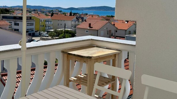Een balkon met een beige parasol, een houten tafel en een witte stoel.