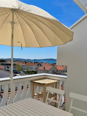 A balcony with a beige umbrella, a wooden table, and a white chair. - Loft Vista Mare (Zadar)