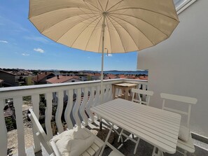 A balcony with a white table and chairs, a beige umbrella, and a view of a residential area. - Loft Vista Mare (Zadar)