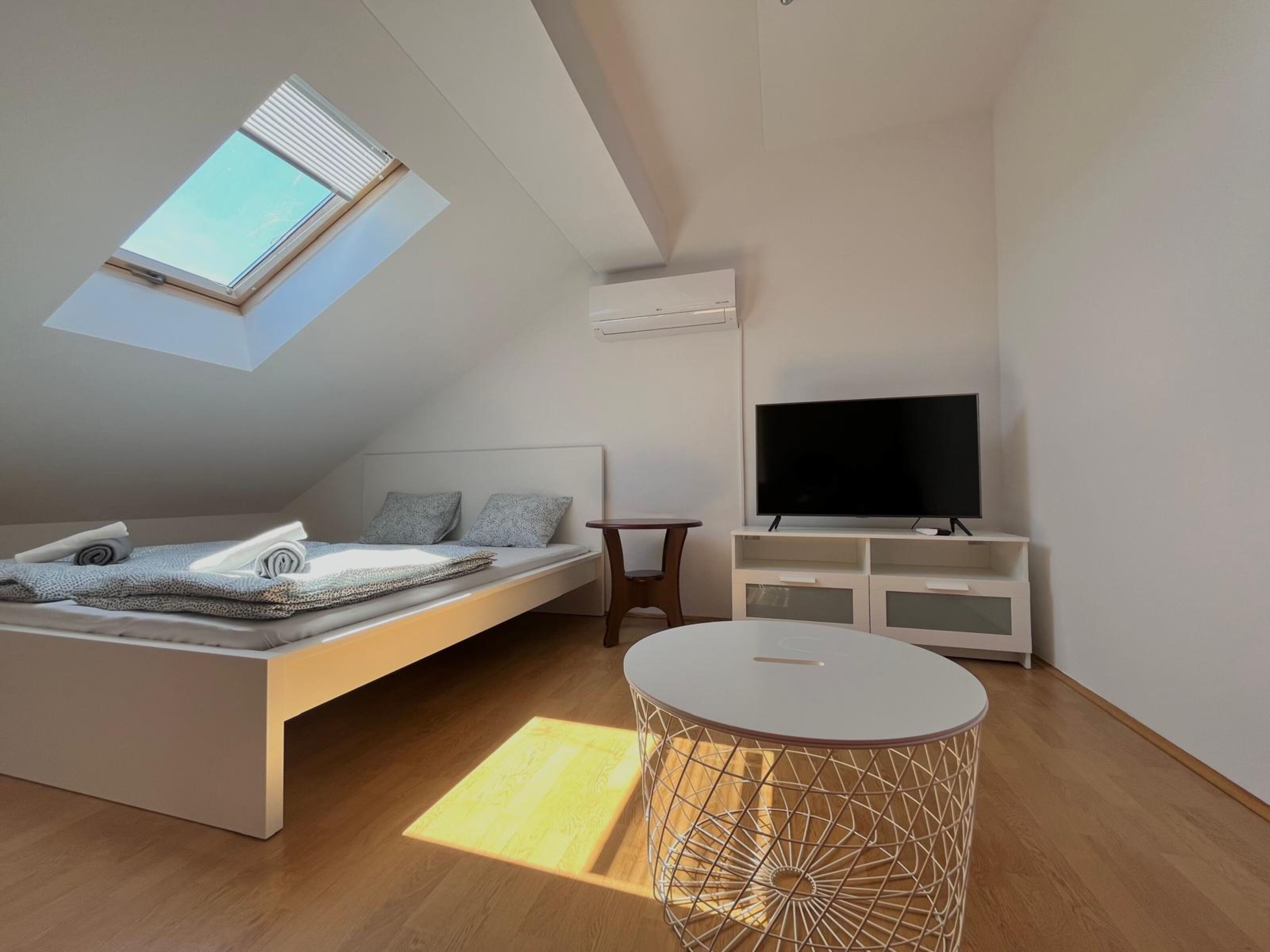 A modern bedroom with a loft bed, a flat-screen TV, a small table, and a unique geometric coffee table.