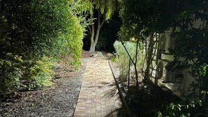 A paved pathway in a garden area with trees and shrubs on either side. - Bordeaux 45 (Cape Town)